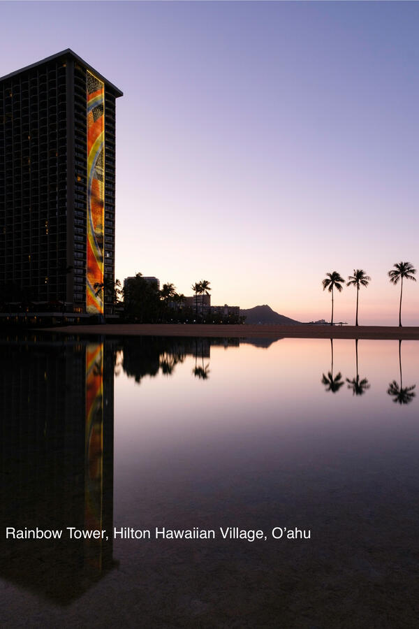 Iconic Rainbow Tower Hawaiian resort at sunset with palm trees reflected in water